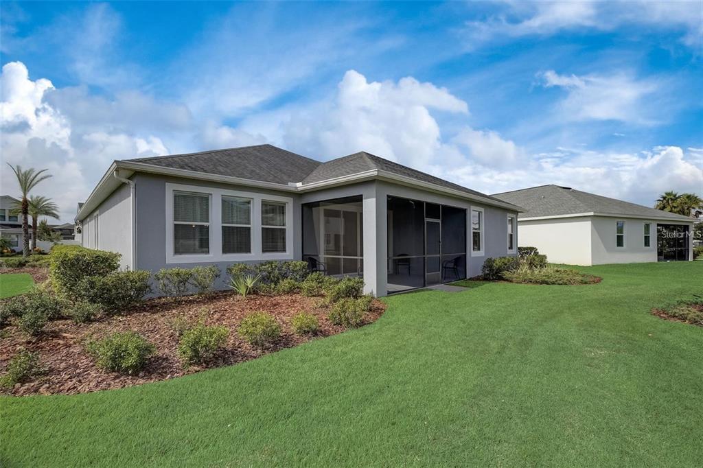 A gray house with a screened-in back porch and a landscaped yard under a blue sky — 4693 FAIRY TALE CIRCLE, KISSIMMEE, FL