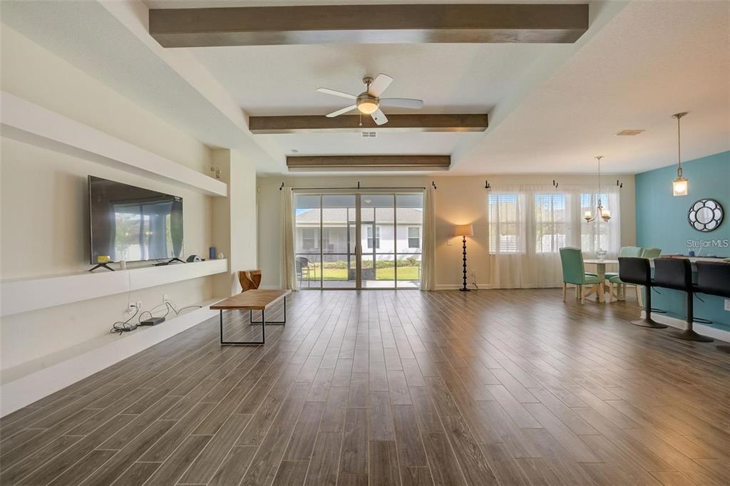 A spacious living and dining area features wood-look tile floors, ceiling beams, and sliding doors — 4693 FAIRY TALE CIRCLE, KISSIMMEE, FL