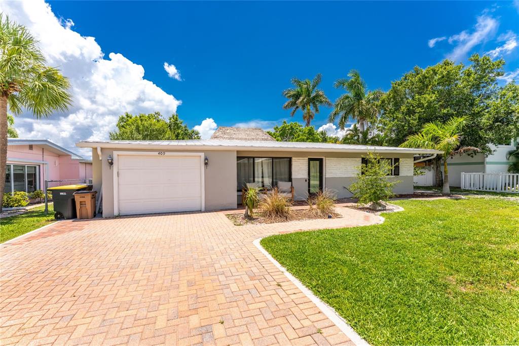 A single-story house with a white garage door, brick paver driveway, and palm trees — 409 W ANN STREET, PUNTA GORDA, FL