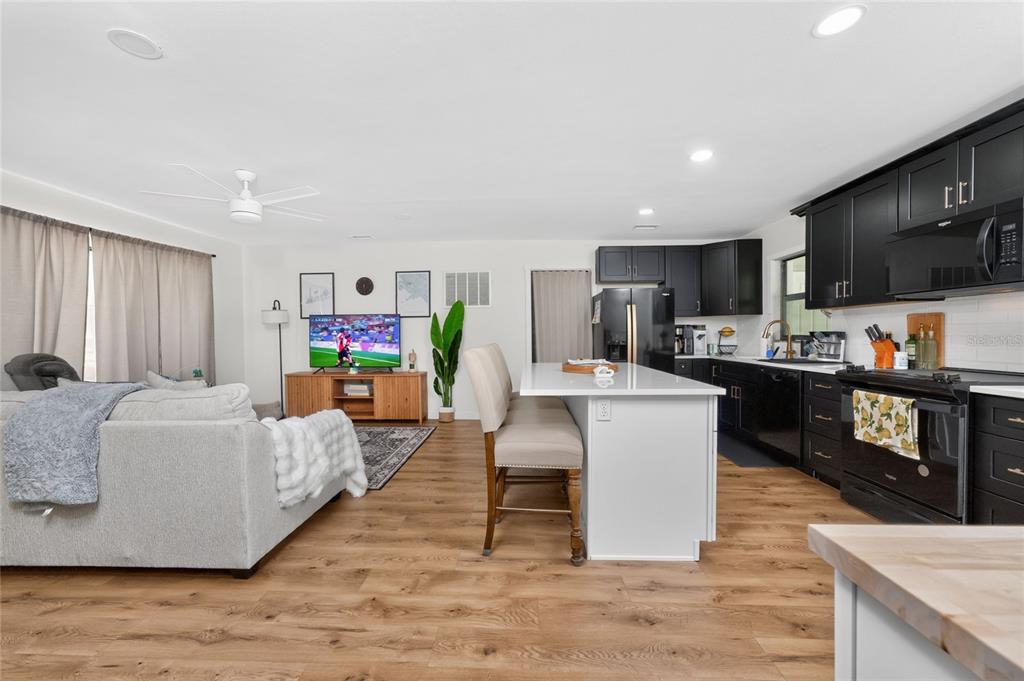An open-concept living room and kitchen featuring wood-look flooring, white cabinets, and a kitchen island — 409 W ANN STREET, PUNTA GORDA, FL