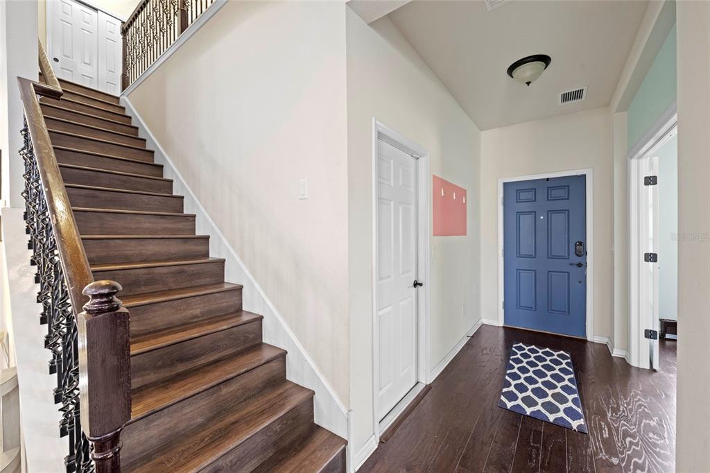 An entryway features a wooden staircase with iron railings, a blue front door, and hardwood floors — 10816 79TH STREET E, PARRISH, FL