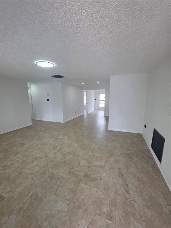 An open-concept living area features white walls, a textured ceiling, and light-colored tile flooring — 8948 SAINT REGIS LANE, PORT RICHEY, FL