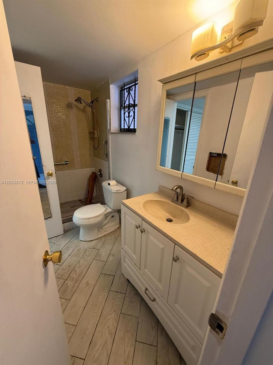 A bathroom features a white vanity, a toilet, a walk-in shower, and wood-look tile flooring — 18555 NE 14th Ave # 615A, Miami FL 33179, MIAMI, FL