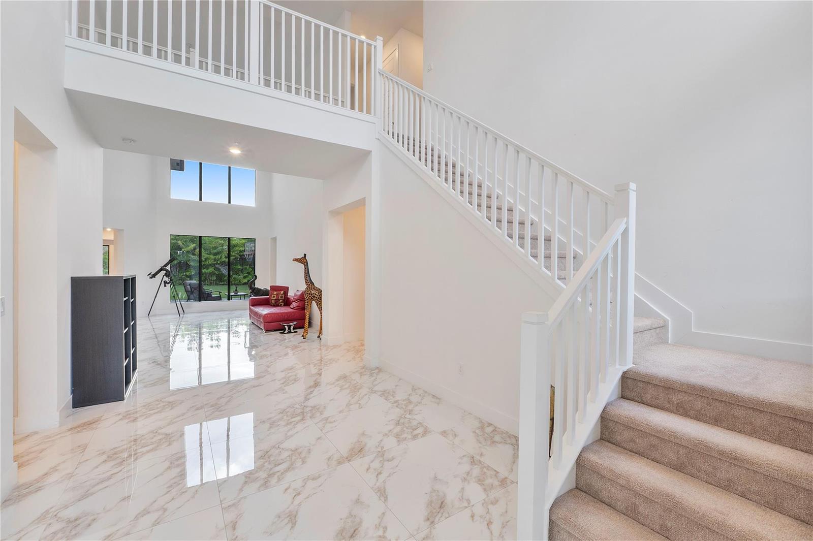 A bright, two-story foyer features white marble floors, a carpeted staircase, and a red sofa — 10472 Cobalt Court, Parkland FL 33076, PARKLAND, FL