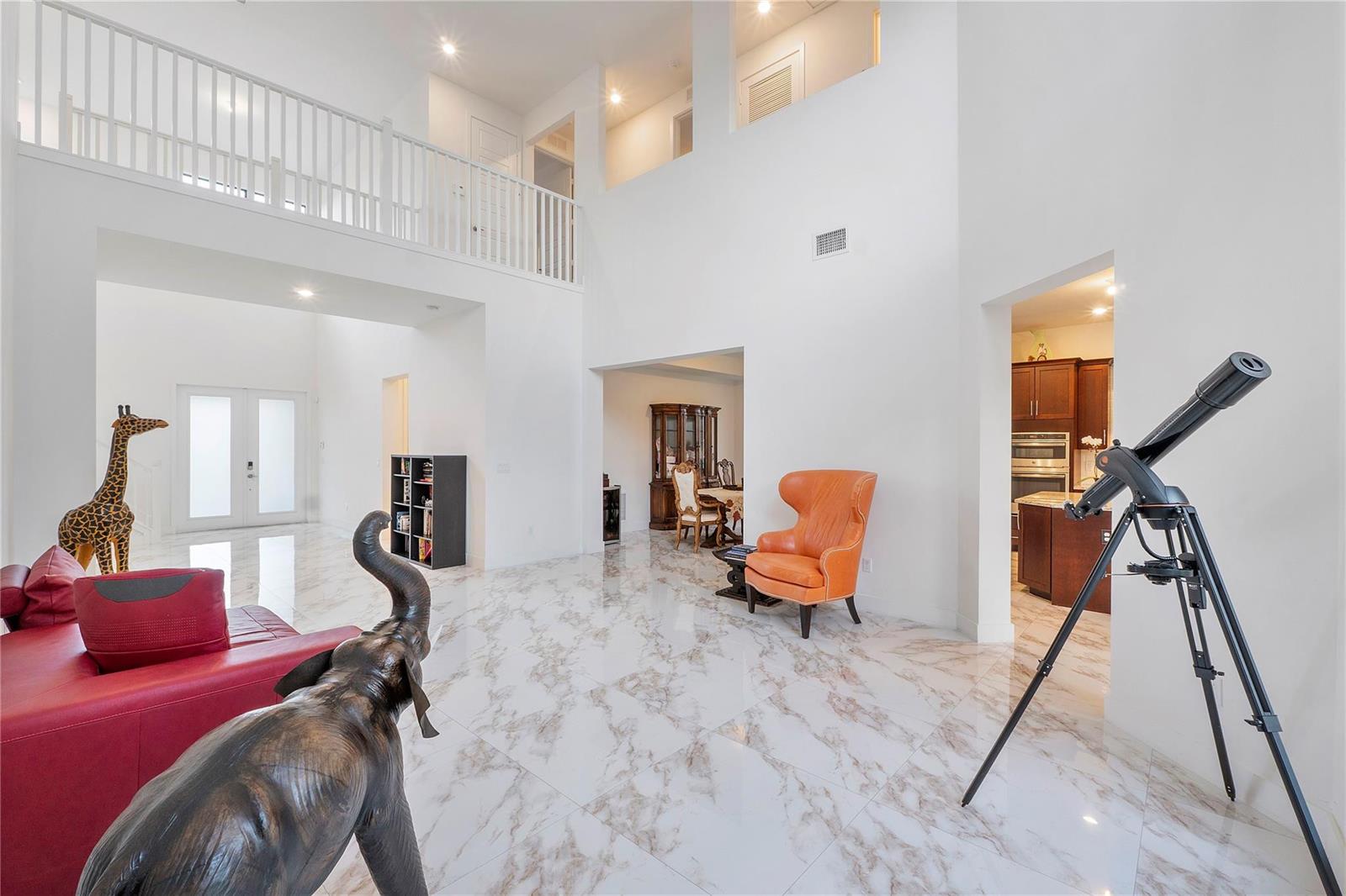 A bright, high-ceilinged living area features white marble floors, an orange chair, and animal statues — 10472 Cobalt Court, Parkland FL 33076, PARKLAND, FL