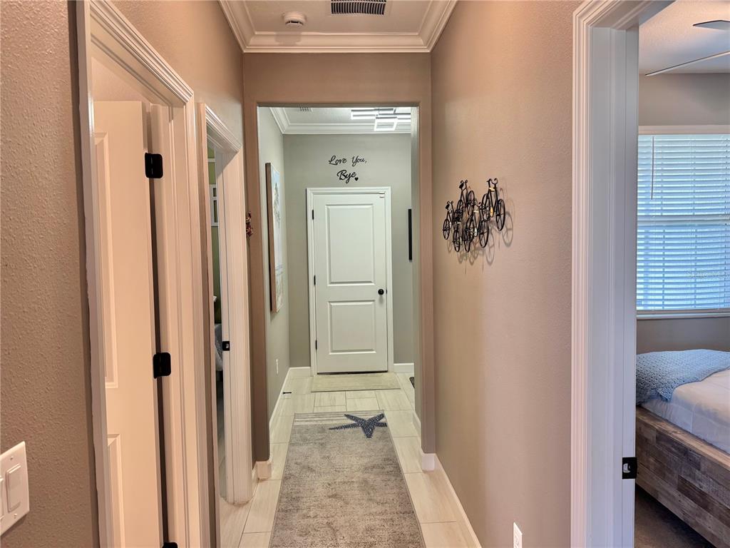 A hallway with light tile flooring leads to a white door with wall art — 12842 LILY QUARTZ LOOP, PARRISH, FL