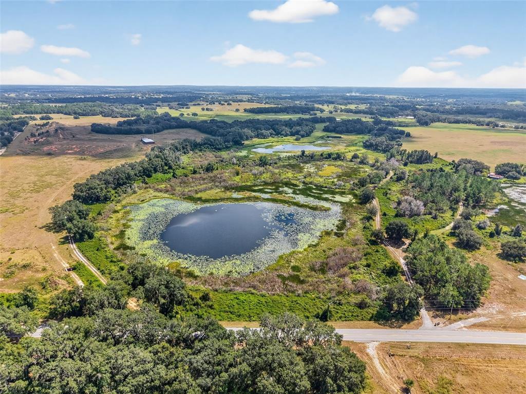 An aerial view shows a large pond surrounded by trees, fields, and a paved road — COUNTY ROAD 48, GROVELAND, FL
