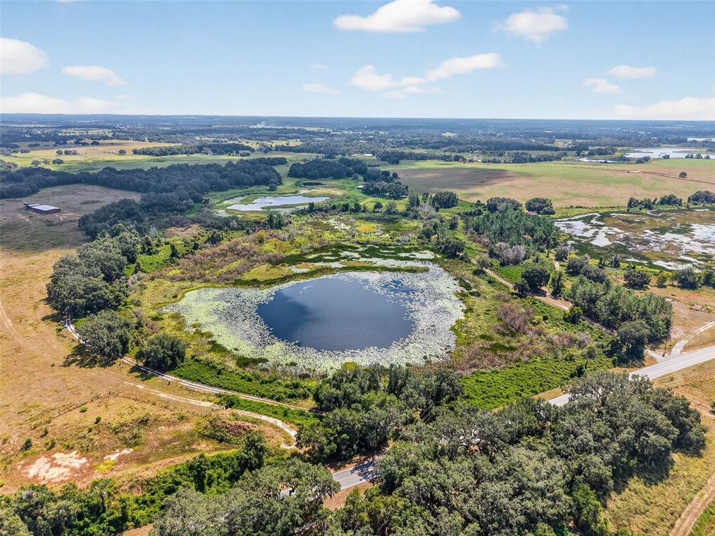 An aerial view shows a pond surrounded by trees and fields near a paved road — COUNTY ROAD 48, GROVELAND, FL