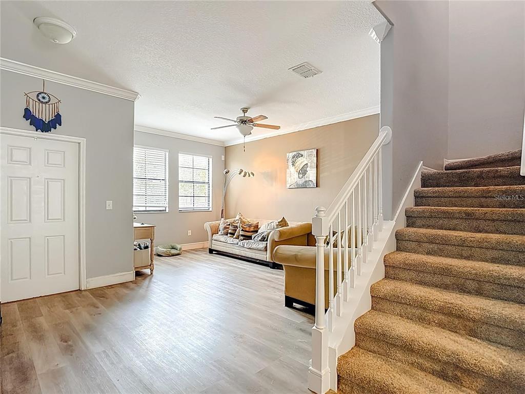 A living room features light wood-look flooring, a tan sofa, and carpeted stairs with railings — 4442 FENNWOOD COURT, WESLEY CHAPEL, FL