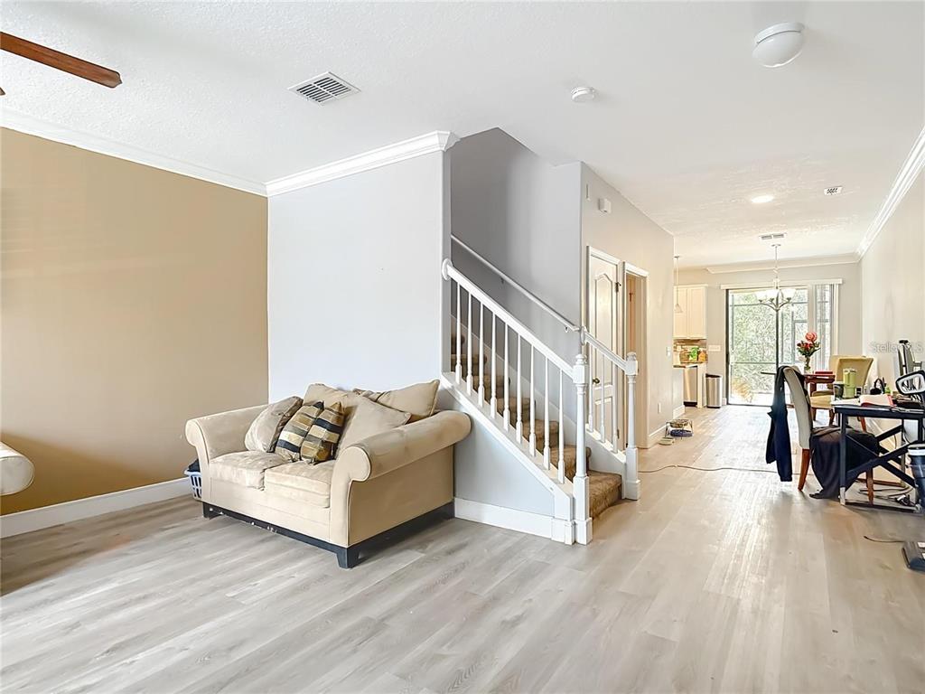 A living room with light wood-look flooring, a beige sofa, and a staircase — 4442 FENNWOOD COURT, WESLEY CHAPEL, FL