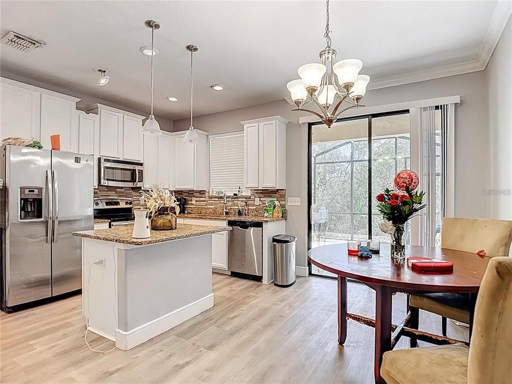 A kitchen with white cabinets, granite countertops, stainless steel appliances, and an adjacent dining area — 4442 FENNWOOD COURT, WESLEY CHAPEL, FL