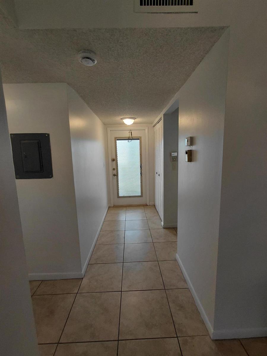 A hallway with beige tile flooring leads to a glass-paneled exterior door — 6850 Royal Palm Boulevard # G211, Margate FL 33063, MARGATE, FL