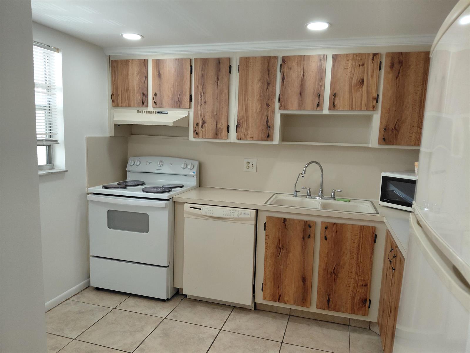 A kitchen with white appliances, wood-grain cabinet doors, beige countertops, and light-colored tile flooring — 6850 Royal Palm Boulevard # G211, Margate FL 33063, MARGATE, FL