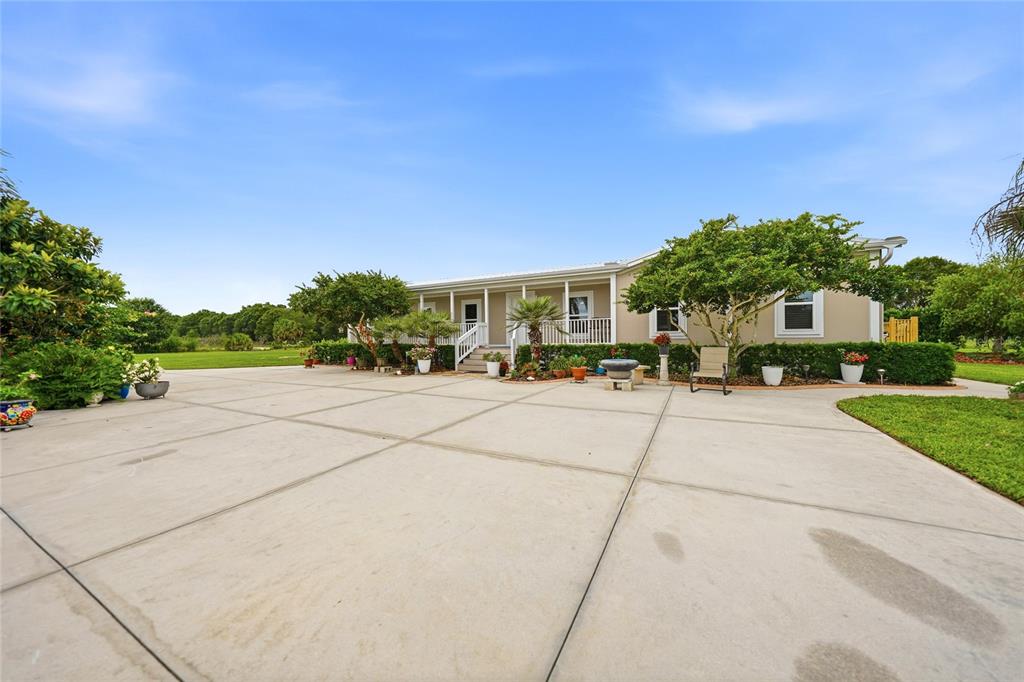 A single-story house with a covered porch sits behind a large concrete driveway — 11354 SE SOUTH HOG BAY AVENUE, ARCADIA, FL