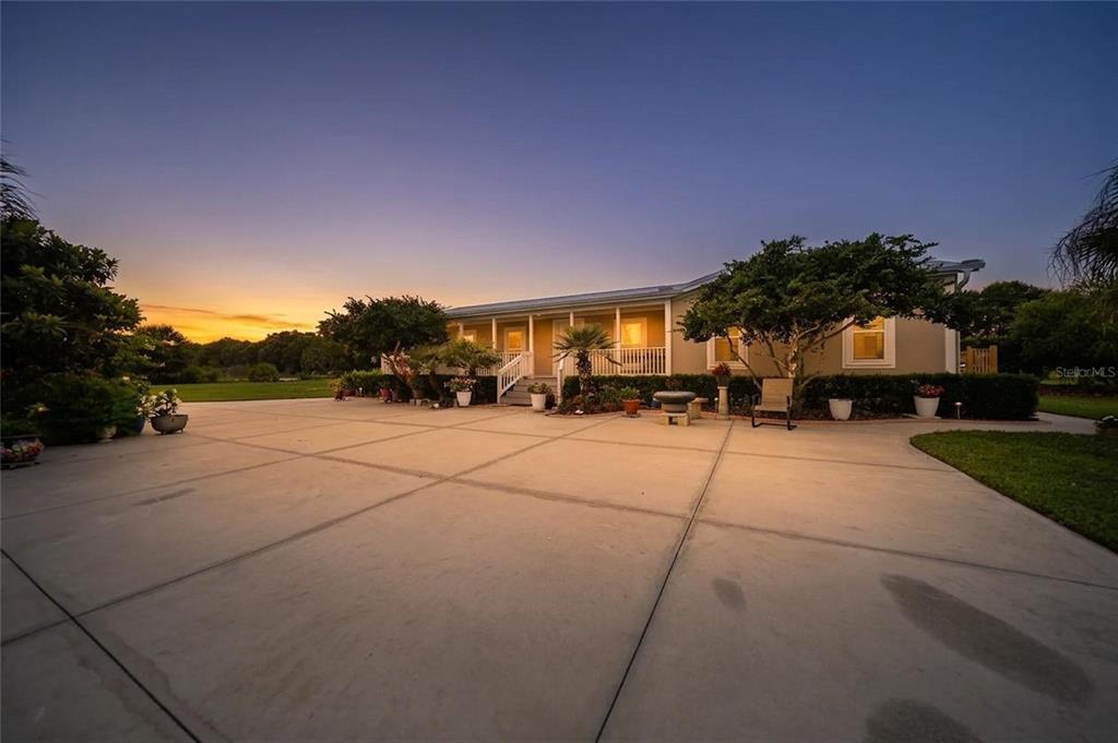 A single-story house with a large concrete driveway and a covered front porch at sunset — 11354 SE SOUTH HOG BAY AVENUE, ARCADIA, FL