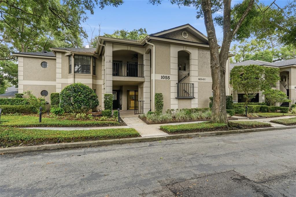 A two-story apartment building exterior features tan stucco walls, a covered entryway, and balconies — 1055 N KENSINGTON PARK DRIVE S UNIT 612, ALTAMONTE SPRINGS, FL