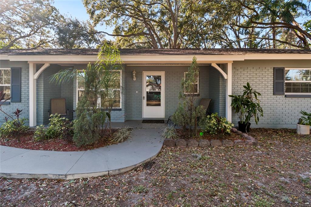 A gray brick house with a covered front porch, a concrete walkway, and mature trees — 9628 DAVIS ROAD, TAMPA, FL