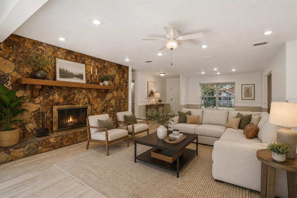 A living room with light wood-look tile flooring, a stone fireplace, and sliding glass doors — 9628 DAVIS ROAD, TAMPA, FL