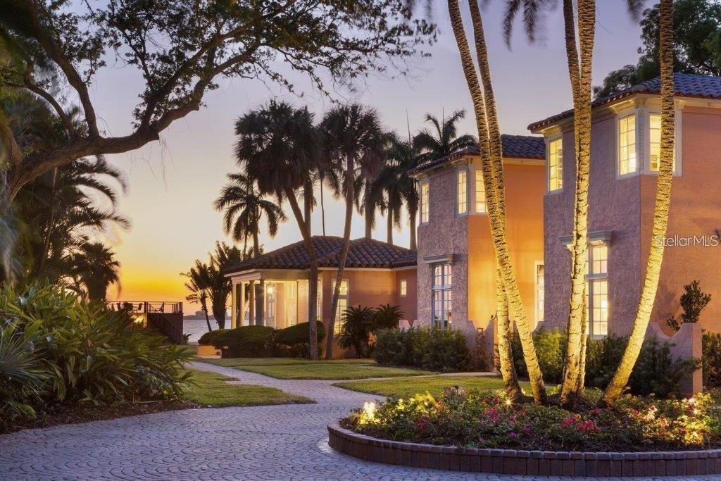A multi-story stucco house with a paved driveway, palm trees, and a sunset waterfront view — 4511 BAY SHORE ROAD, SARASOTA, FL