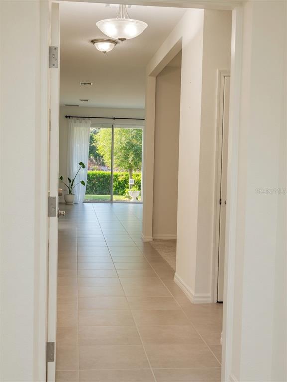 A tiled hallway leads to a living area with sliding glass doors overlooking a backyard — 17589 GARSALASO CIR, BROOKSVILLE, FL