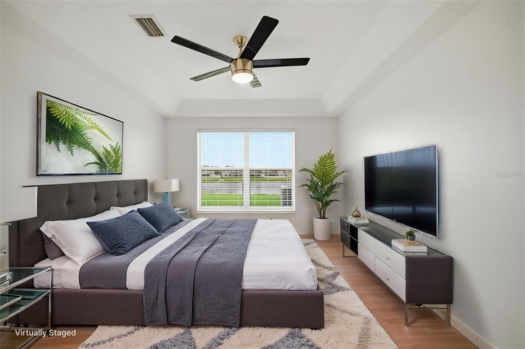 A bedroom features a gray upholstered bed, a wall-mounted television, and a ceiling fan — 10604 LAKESIDE VISTA DRIVE, RIVERVIEW, FL