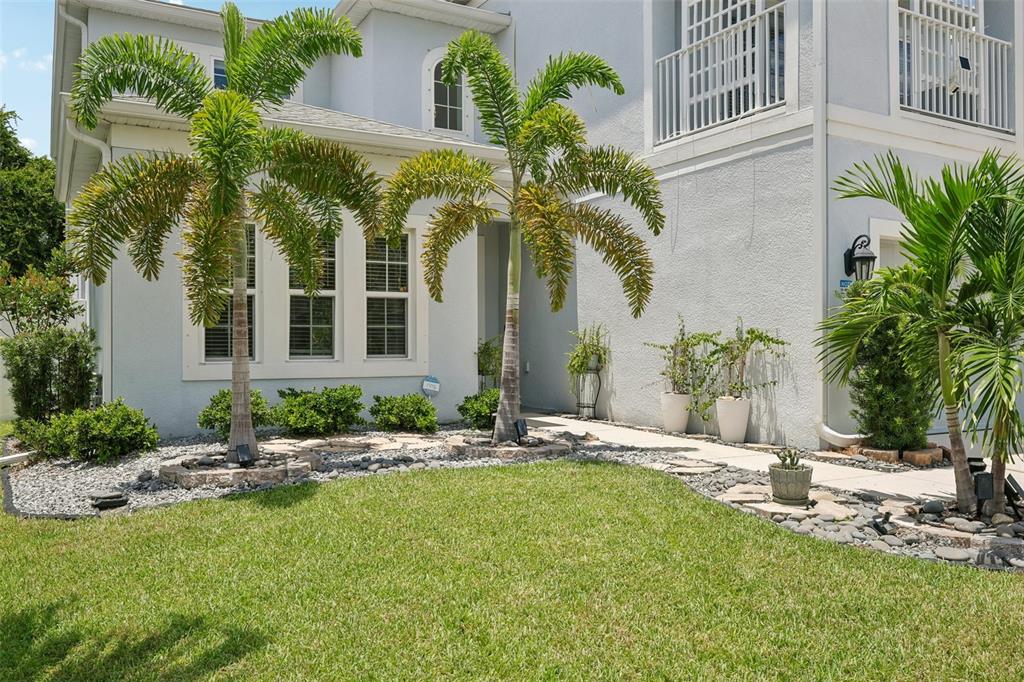 A light-colored house exterior features palm trees, a stone-bordered garden, and a grassy lawn — 9085 SPRUCE CREEK CIRCLE, RIVERVIEW, FL