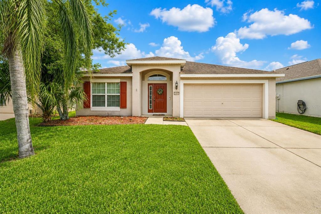 A single-story house with a beige exterior, a two-car garage, and a red front door — 14450 WAKE ROBIN DRIVE, BROOKSVILLE, FL