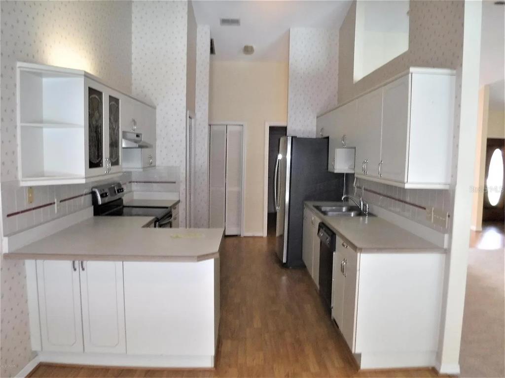A kitchen features white cabinets, light countertops, a black refrigerator, and a patterned wallpaper — 105 MARBLED GODWIT COURT, DAYTONA BEACH, FL