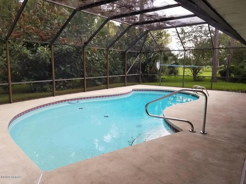 A screened-in swimming pool with a concrete deck and a metal handrail — 105 MARBLED GODWIT COURT, DAYTONA BEACH, FL