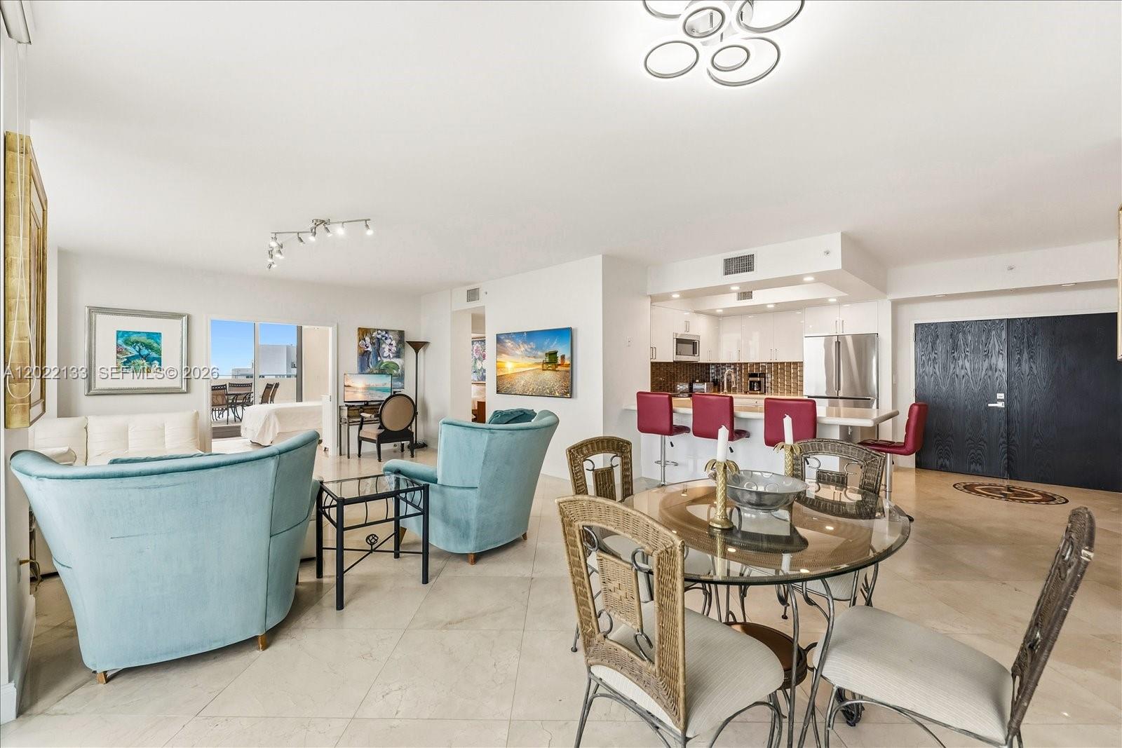 An open-concept living and dining area features light tile floors, blue armchairs, and a kitchen — 90 Alton Rd, Miami Beach FL 33139, MIAMI BEACH, FL