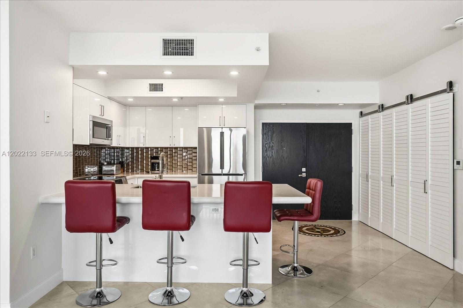 A modern kitchen features white cabinetry, a breakfast bar with red stools, and tile flooring — 90 Alton Rd, Miami Beach FL 33139, MIAMI BEACH, FL