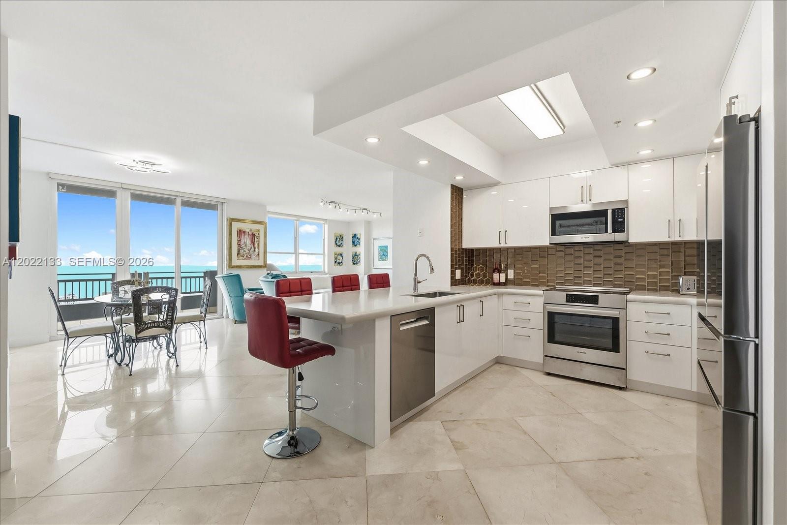 A modern kitchen with white cabinets and a breakfast bar overlooks a dining area — 90 Alton Rd, Miami Beach FL 33139, MIAMI BEACH, FL