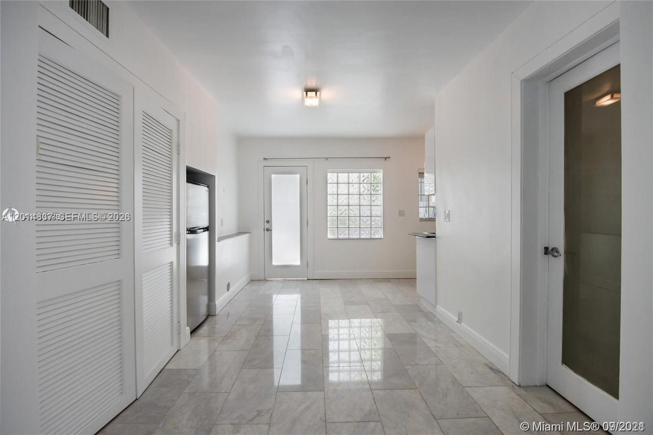 A bright kitchen features white walls, tile flooring, louvered closet doors, and a glass-paneled door — 928 Jefferson Ave, Miami Beach FL 33139, MIAMI BEACH, FL