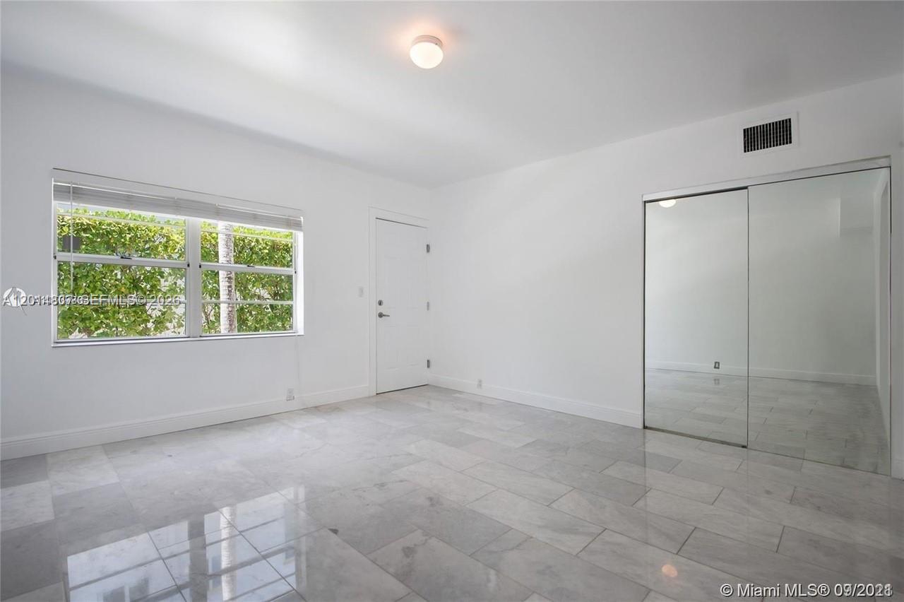 A bright, empty bedroom features white walls, marble-style tile flooring, and mirrored closet doors — 928 Jefferson Ave, Miami Beach FL 33139, MIAMI BEACH, FL