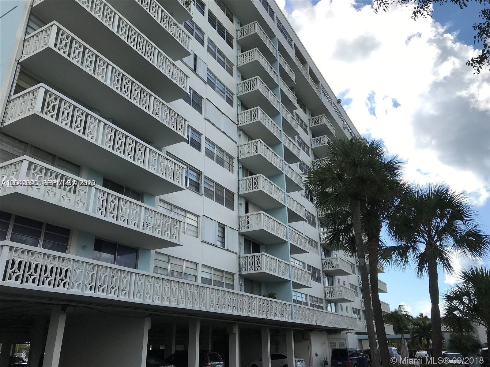 A multi-story apartment building features white balconies with decorative railings and a ground-level parking area — 13155 Ixora Ct # 810, North Miami FL 33181, NORTH MIAMI, FL