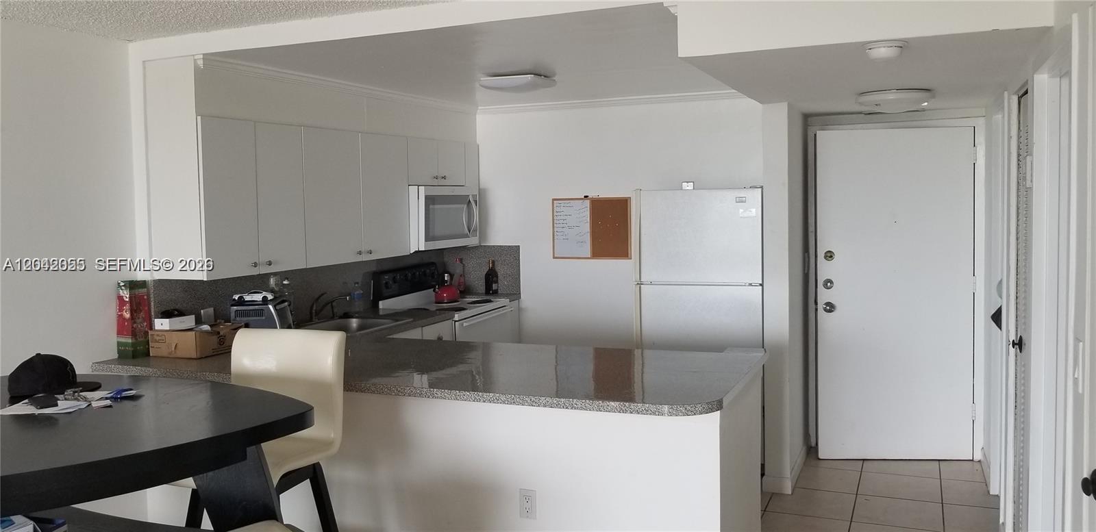 A kitchen features white cabinets, a granite countertop, and a white refrigerator — 13155 Ixora Ct # 810, North Miami FL 33181, NORTH MIAMI, FL