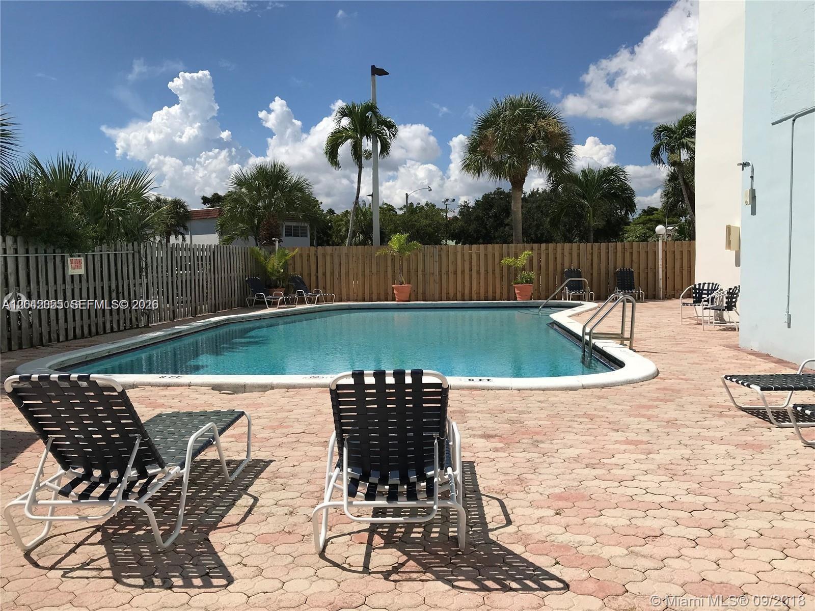 An outdoor swimming pool is surrounded by a paved deck with lounge chairs and fencing — 13155 Ixora Ct # 810, North Miami FL 33181, NORTH MIAMI, FL