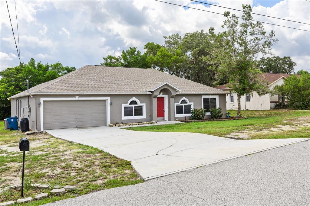 A single-story house with a gray exterior, a red front door, and a concrete driveway — 352 CLEARFIELD AVENUE, SPRING HILL, FL