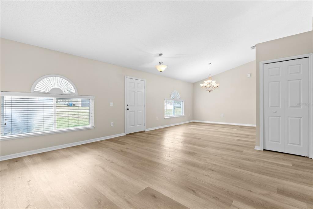 An empty living room features light wood-look flooring, white walls, a vaulted ceiling, and arched windows — 352 CLEARFIELD AVENUE, SPRING HILL, FL