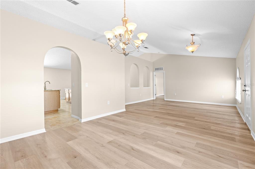 An open living area with light wood flooring, a chandelier, and an arched entryway — 352 CLEARFIELD AVENUE, SPRING HILL, FL
