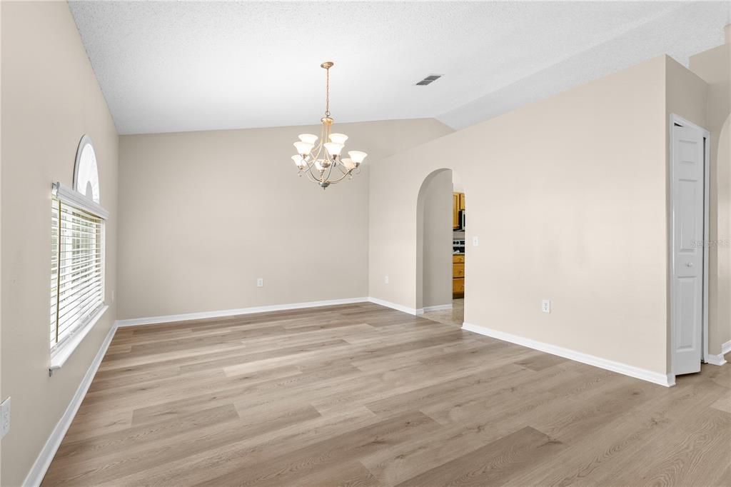 An empty dining room with light wood-look flooring, beige walls, and a central chandelier — 352 CLEARFIELD AVENUE, SPRING HILL, FL