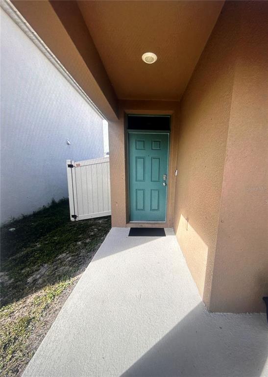 A teal front door is set within a covered concrete entryway next to a fence — 1396 BERRY LANE, DAVENPORT, FL