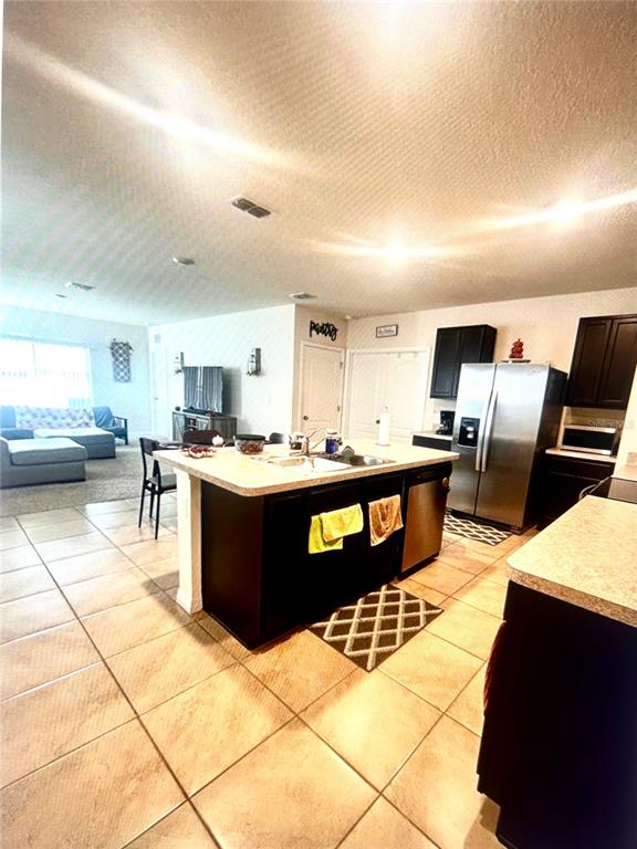 A kitchen with dark cabinets and a central island overlooks an open-concept living area — 1396 BERRY LANE, DAVENPORT, FL