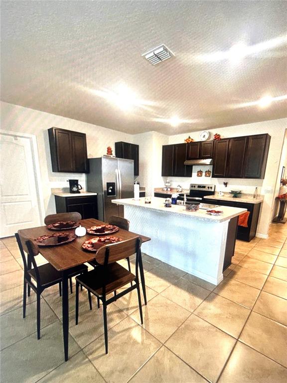 A kitchen features dark wood cabinets, a stainless steel refrigerator, and a dining table — 1396 BERRY LANE, DAVENPORT, FL