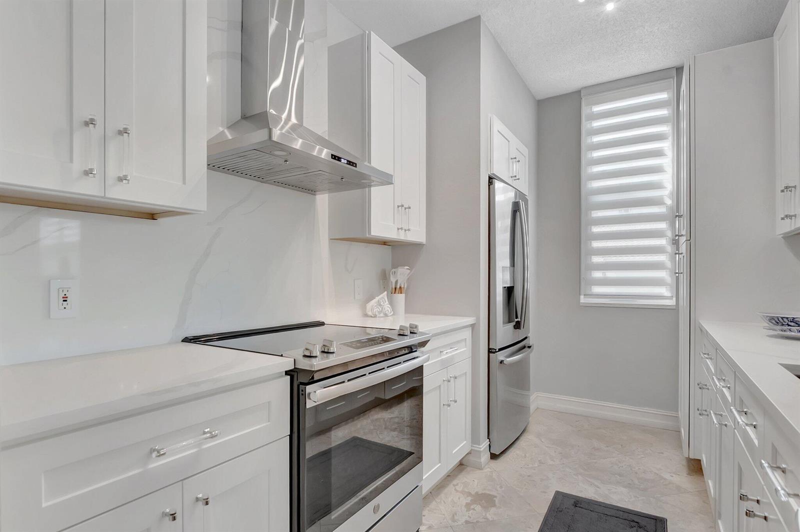 A kitchen features white cabinetry, stainless steel appliances, a marble-style backsplash, and light-colored tile flooring — 3606 S Ocean Boulevard # 108, Highland Beach FL 33487, HIGHLAND BEACH, FL