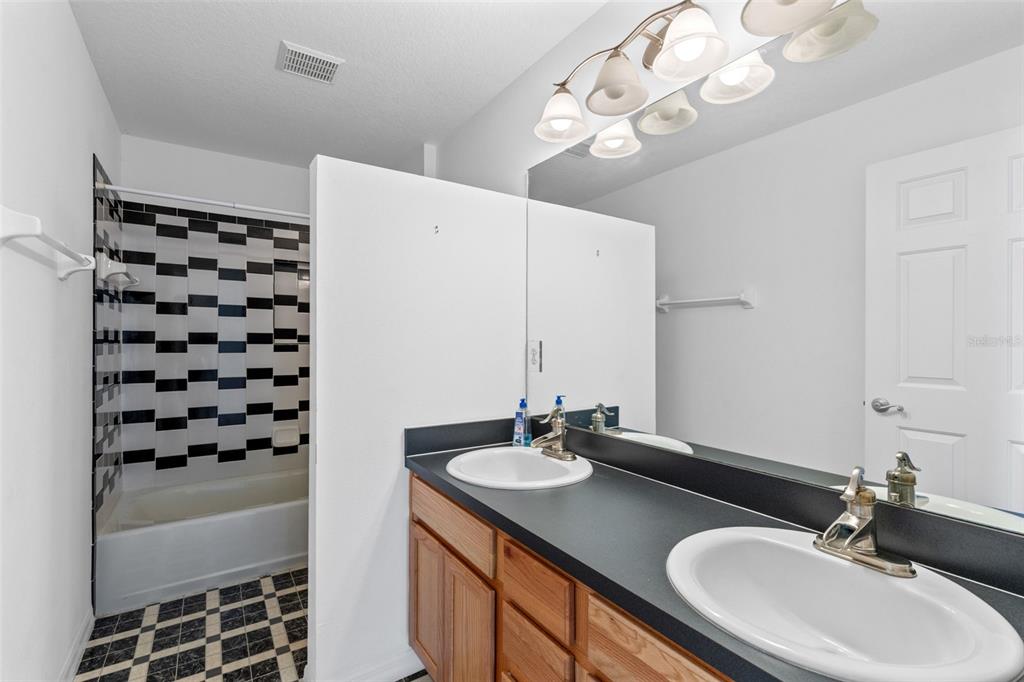 A bathroom features a double vanity with black countertops, wood cabinets, and a tiled tub — 4450 TREASURE CAY ROAD, TAVARES, FL