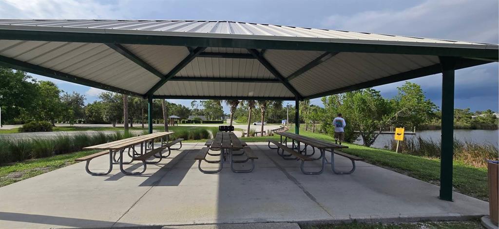 A covered outdoor pavilion features three picnic tables on a concrete slab near a pond — 13879 BEGONIA CIRCLE, PORT CHARLOTTE, FL