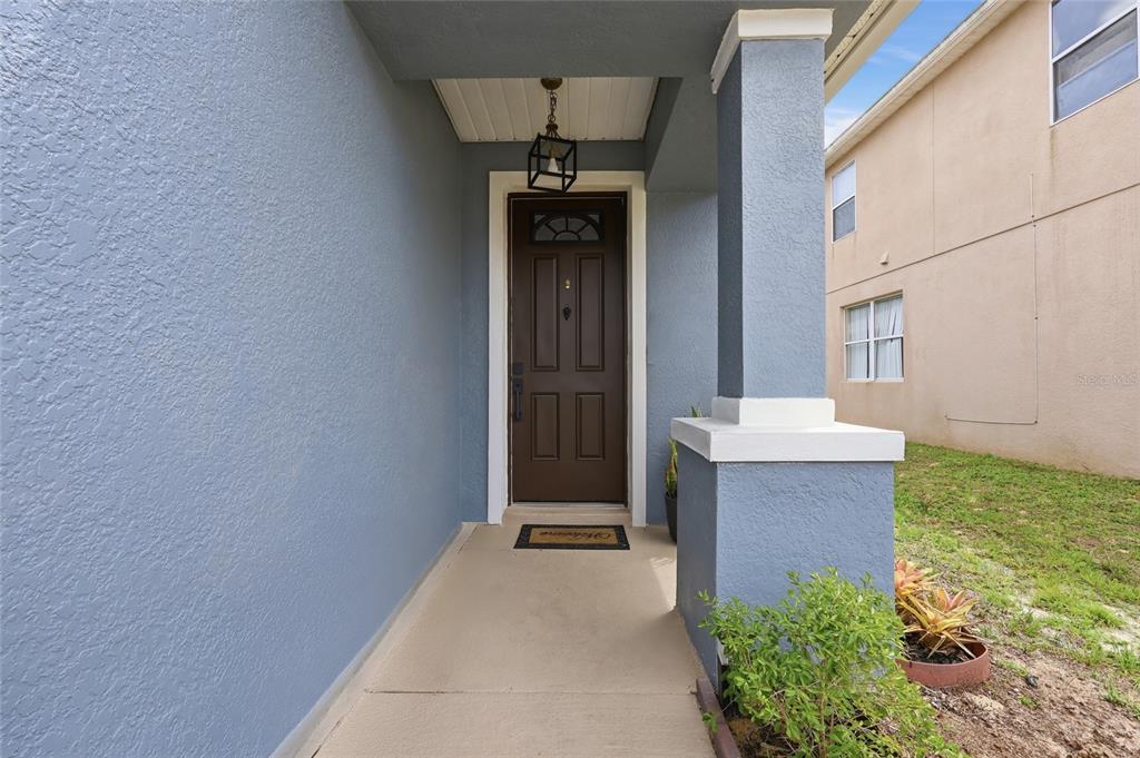 A covered entryway features a brown front door, a hanging lantern, and a concrete porch — 232 ALDRIDGE LANE, DAVENPORT, FL