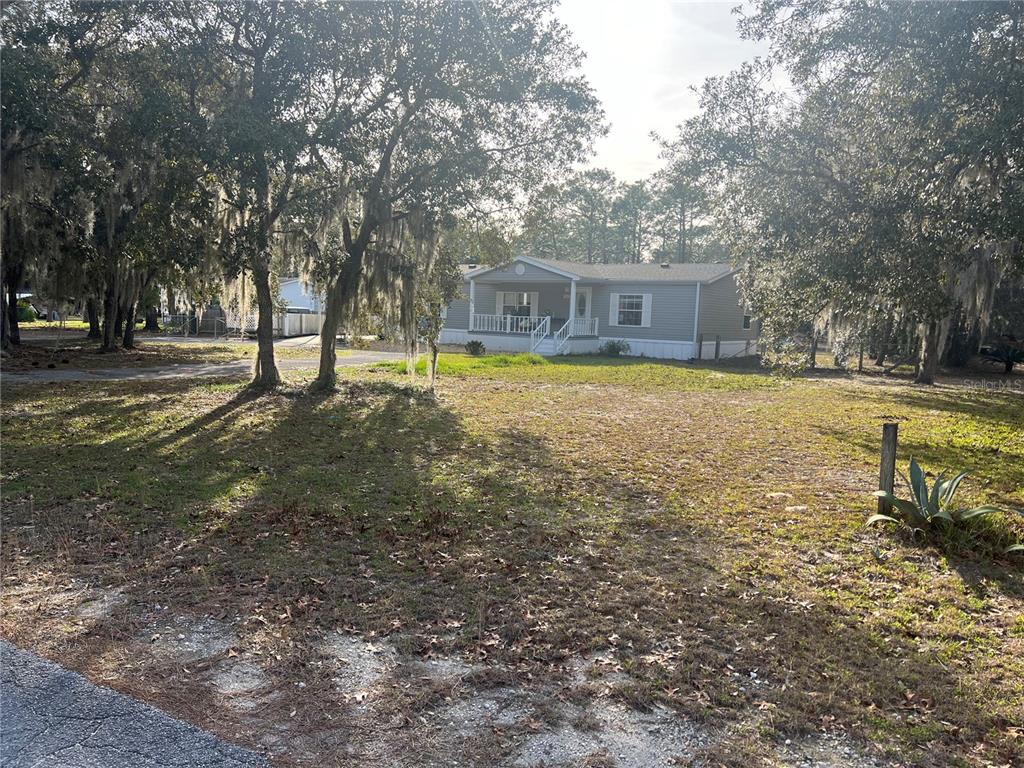 A light-colored manufactured home sits on a grassy lot shaded by large oak trees — 2042 S SUNWOOD POINT, HOMOSASSA, FL