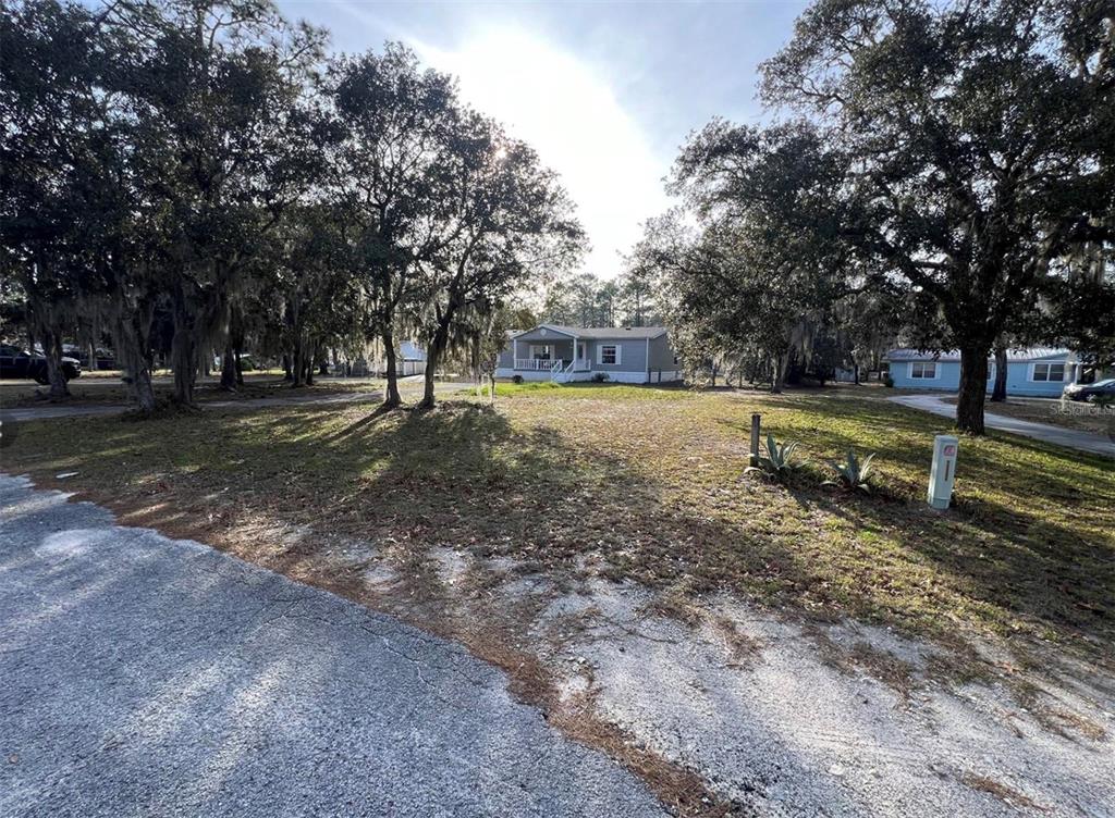 A light-colored manufactured home sits on a grassy lot shaded by large oak trees — 2042 S SUNWOOD POINT, HOMOSASSA, FL